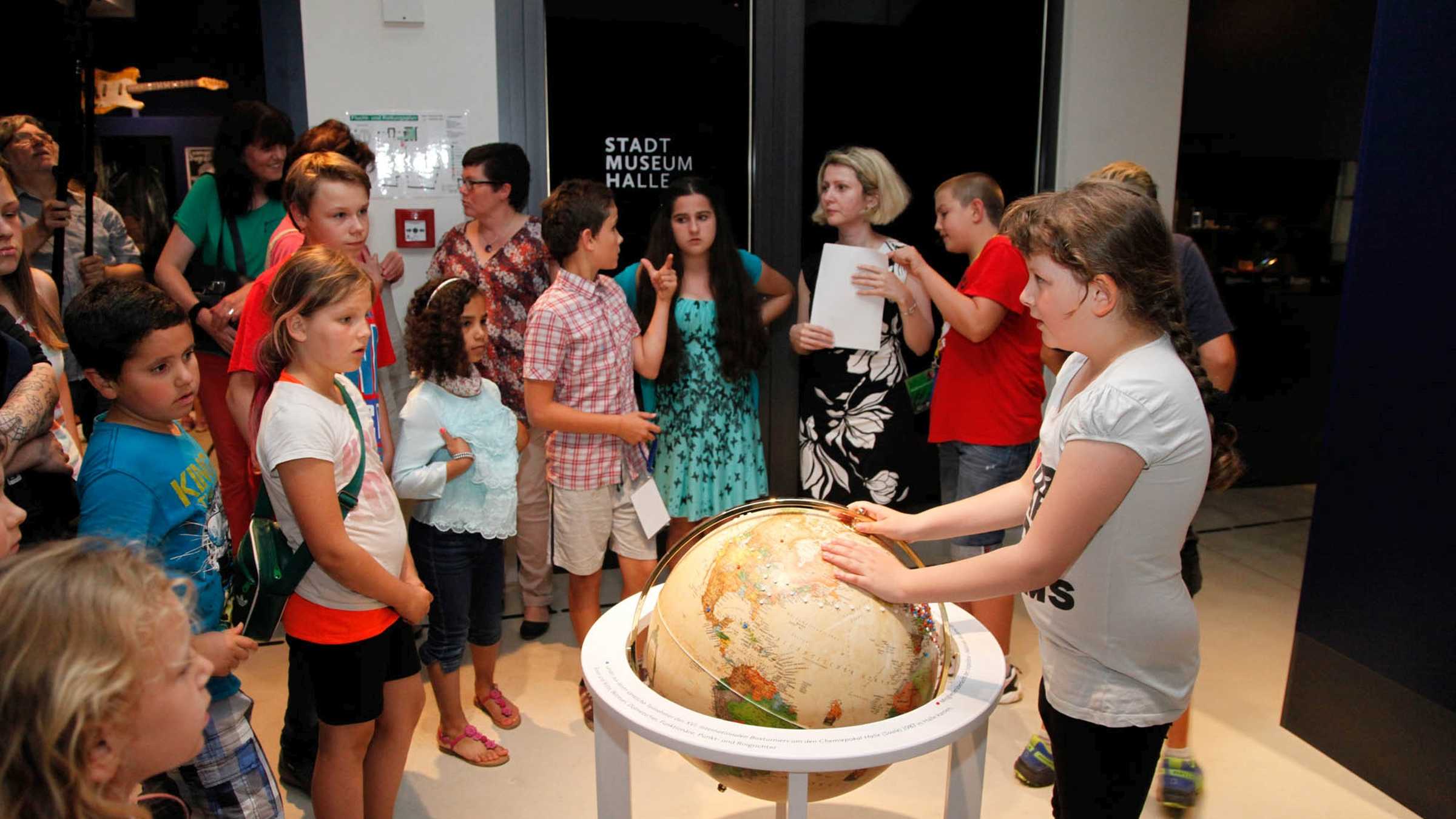 Angebote für Schulen und Kitasa viele Kinder um einen Globus als Ausstellungsstück versammelt