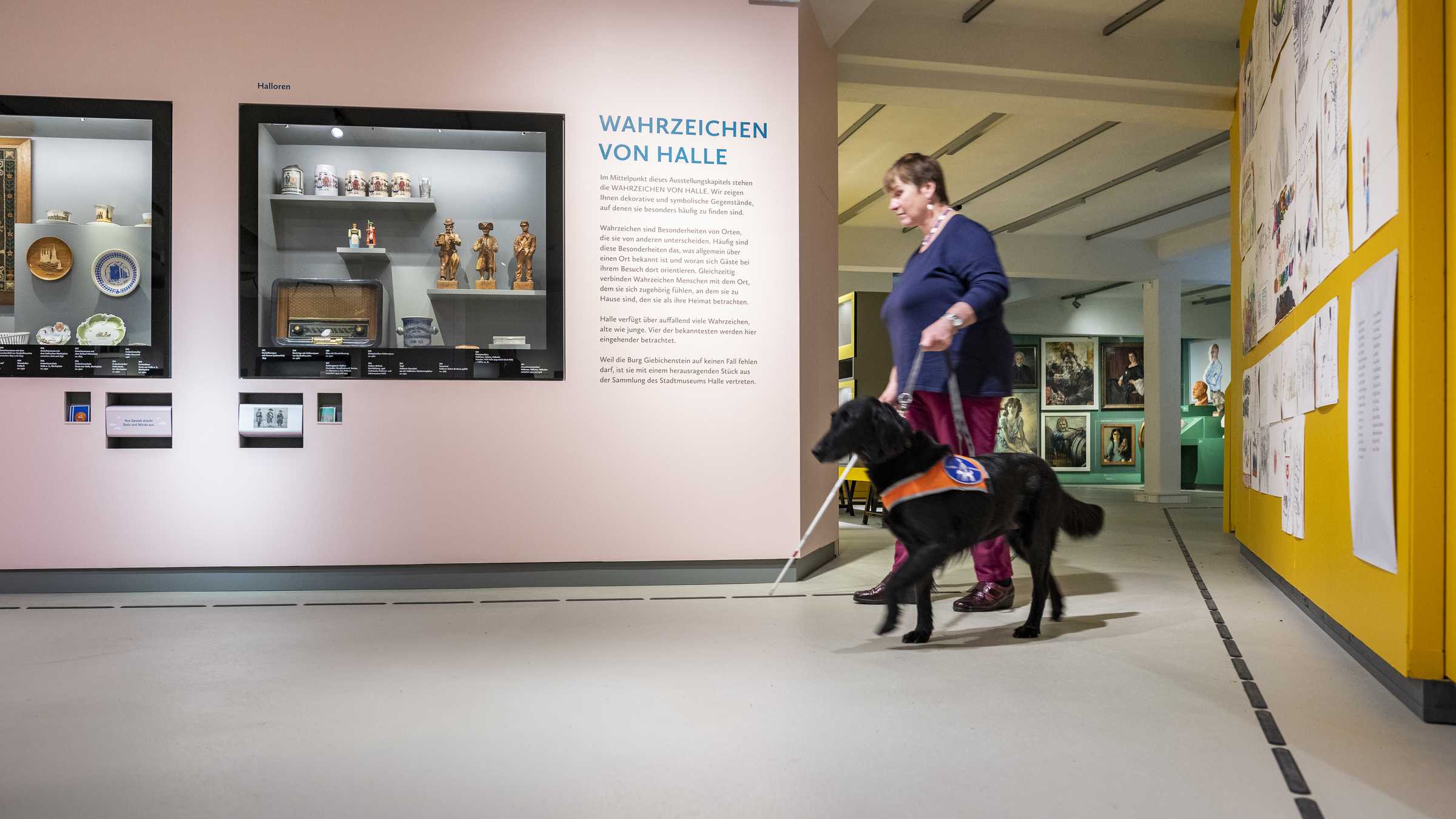 Barrierefreiheit eine Frau begleitet von ihrem schwarzen Blindenhund in der Ausstellung. Diese zeigt die Wahrzeichen von Halle
