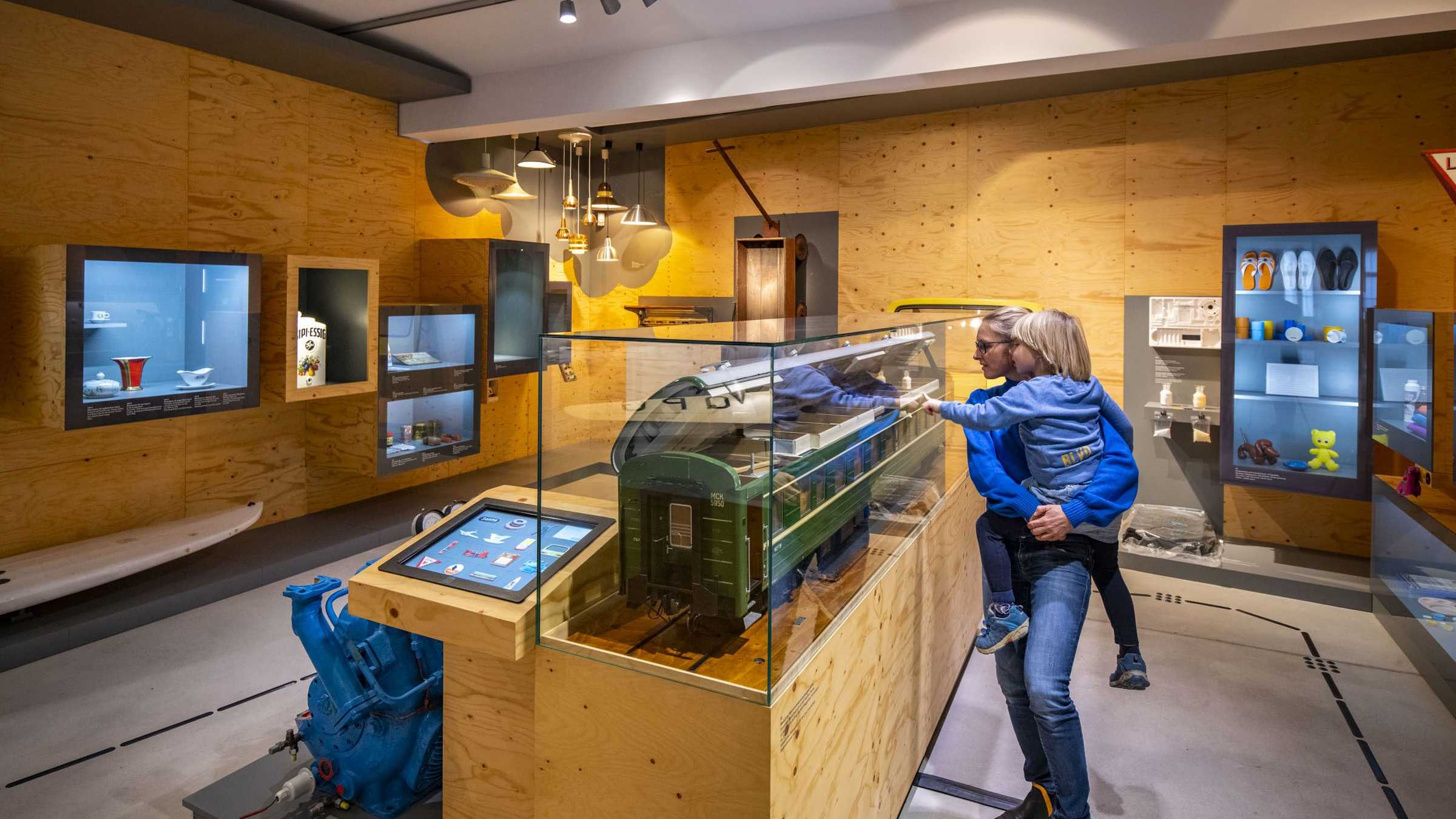 Made in Halle Eine Frau mit einem Kind auf ihrem Arm. Beide schauen sich ein grünes Modell einer Tram in einem Ausstellungsraum an