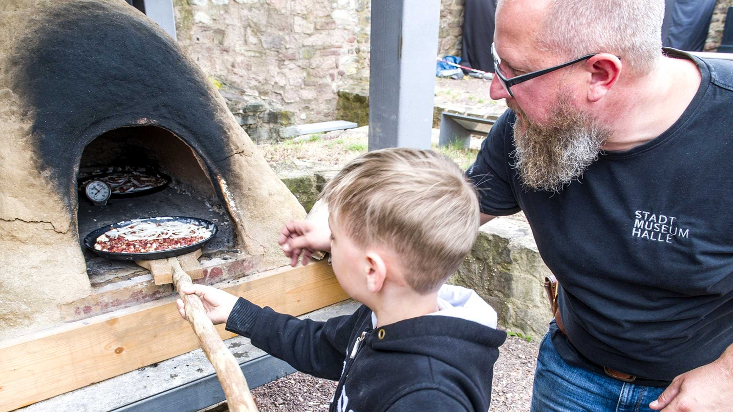 Ein Kind schiebt eine Pizza in den Lehmofen