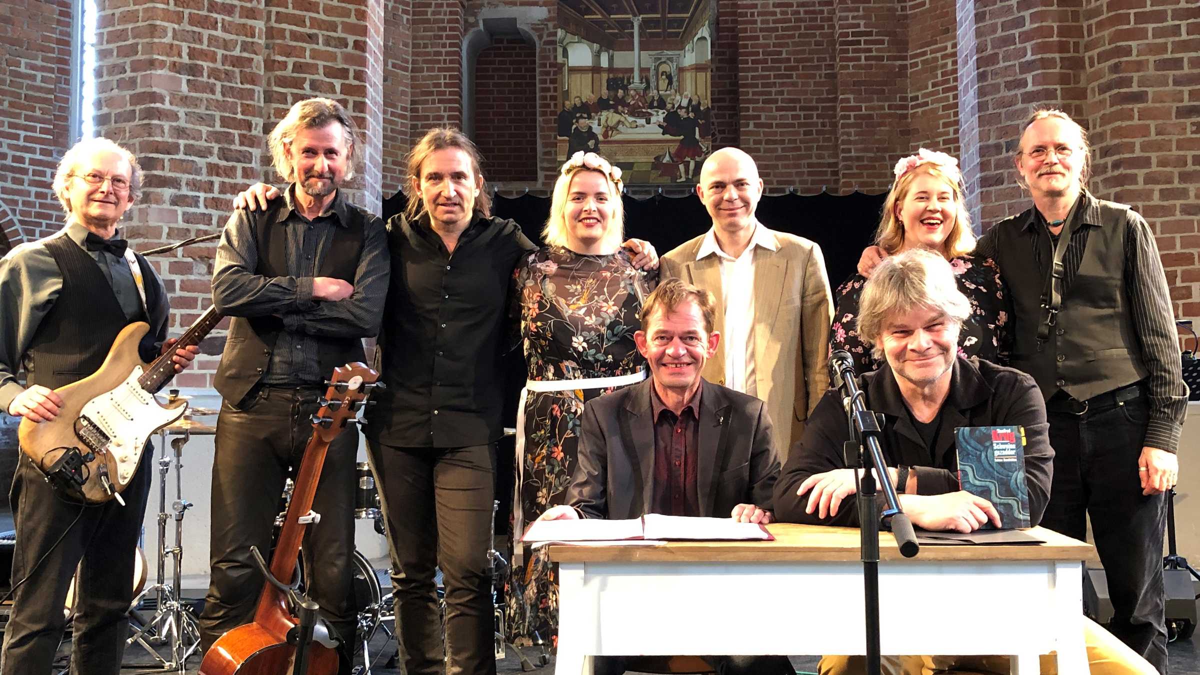 Adolphi singt Krug Ein Foto von acht Personen. Sieben davon stehen und zwei sitzen.