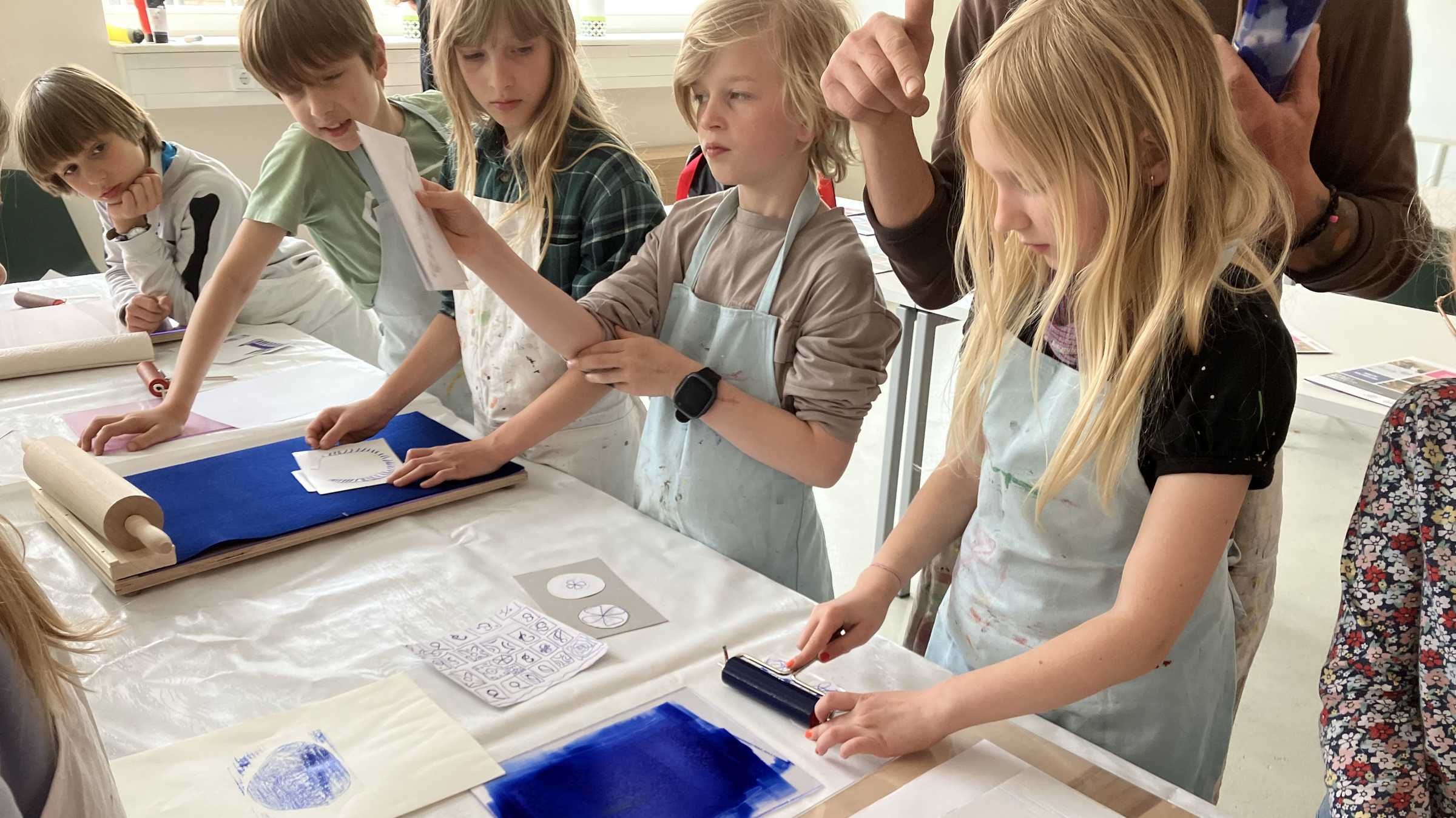 Druckworkshop eine Gruppe von Grundschulkindern steht am Tisch und probiert verschiedene Stufen des Druckvorgangs