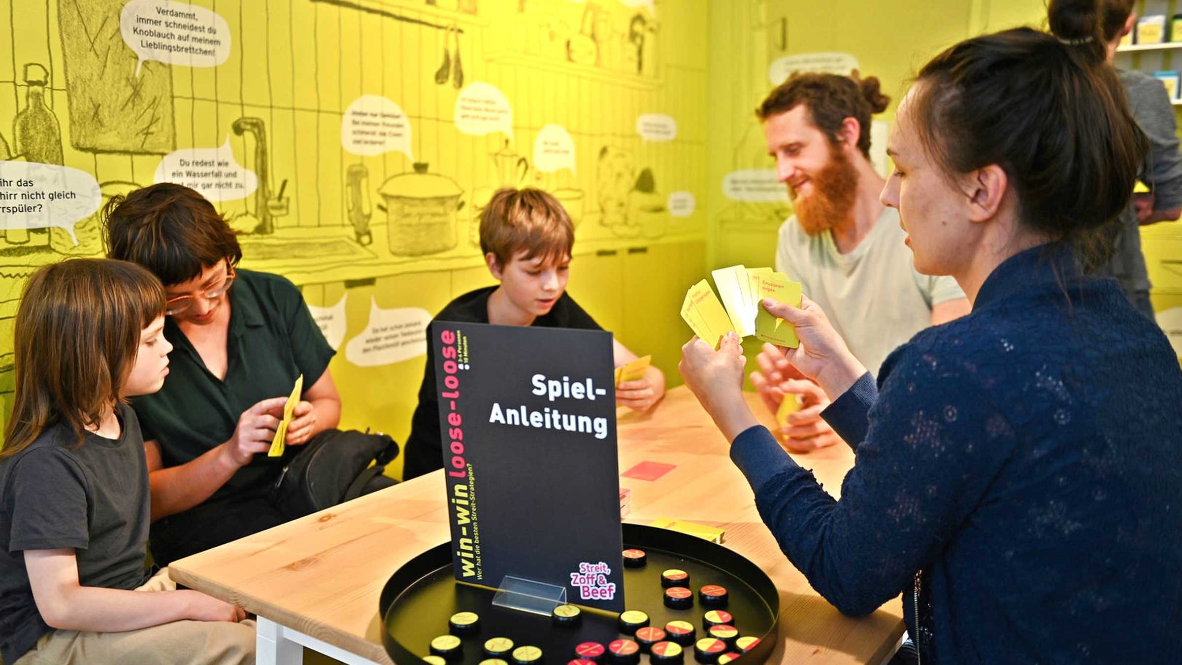 Zwei Frauen, ein Mann und zwei Jungs spielen ein Kartenspiel in der Ausstellung "Streit, Zoff & Beef"