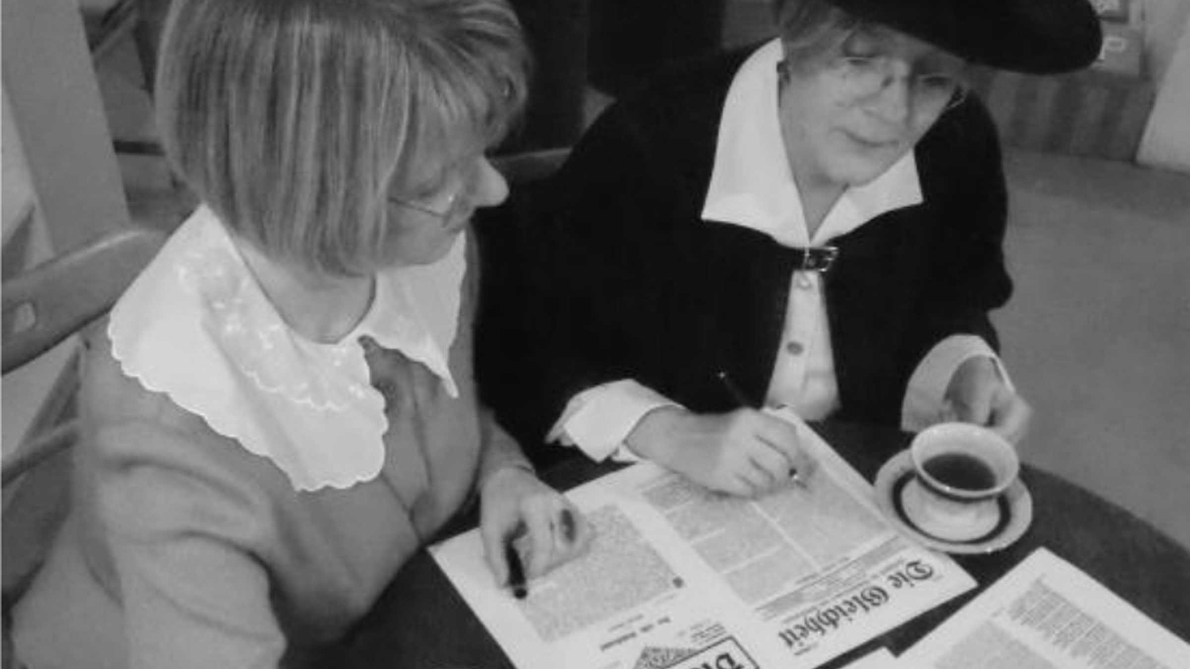 Damenwahl 2 Frauen am Kaffeetisch beugen sich über eine Zeitung