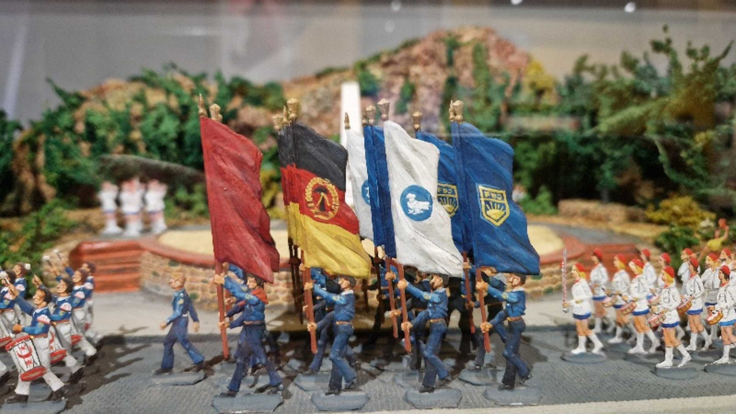Diorama mit Aufmarsch am Denkmal des Kleinen Trompeters Detail aus einem Diorama mit Figuren in FDJ-Hemden, die bei einem Aufmarsch Fahnen tragen