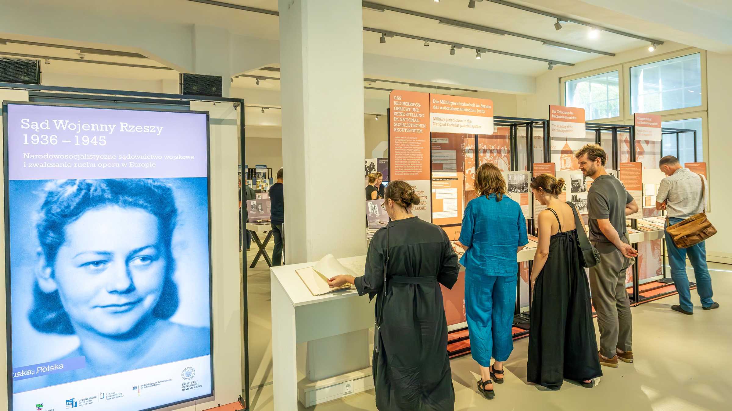 Ausstellung Reichskriegsgericht, Foto: Thomas Ziegler Blick in den Ausstellungsraum mit vielen Menschen und einem Monitor im Vordergrund, der das Portrait einer jungen Frau zeigt