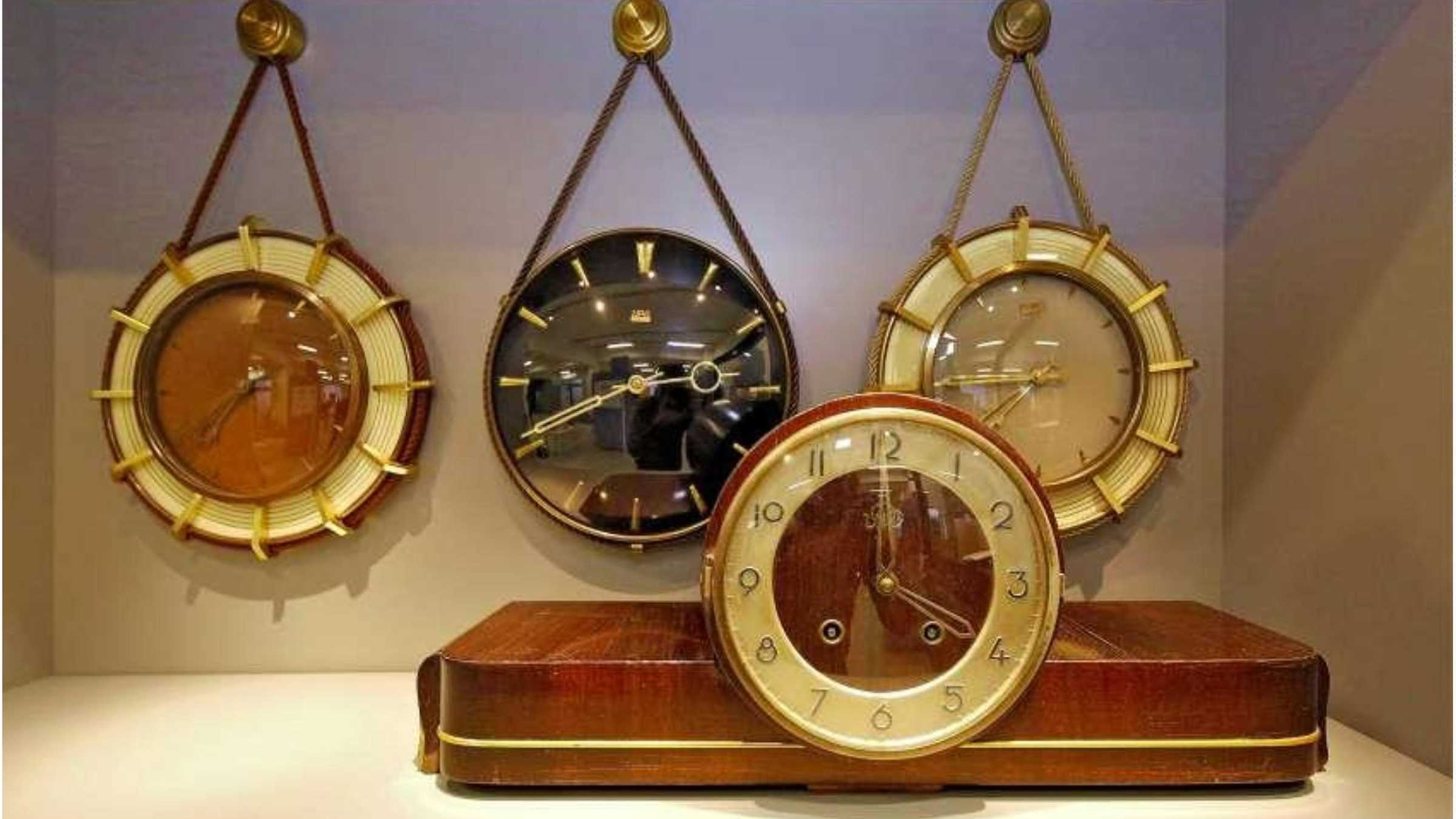 Drei Uhren im Hintergrund an der Wand aufgehängt davor eine Uhr stehend auf der Bdenplatte.