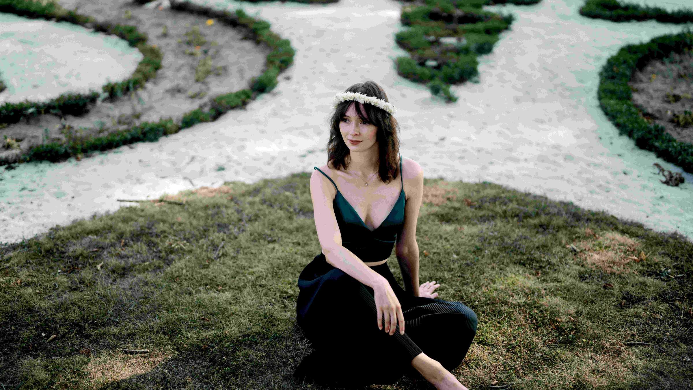 Laura Folker (c) Line Tsoj Luara Folkers sitz in einem dunkelgrünen schulterfreien Kleid und mit Blumenkranz im Haar auf einem Stück Rasen