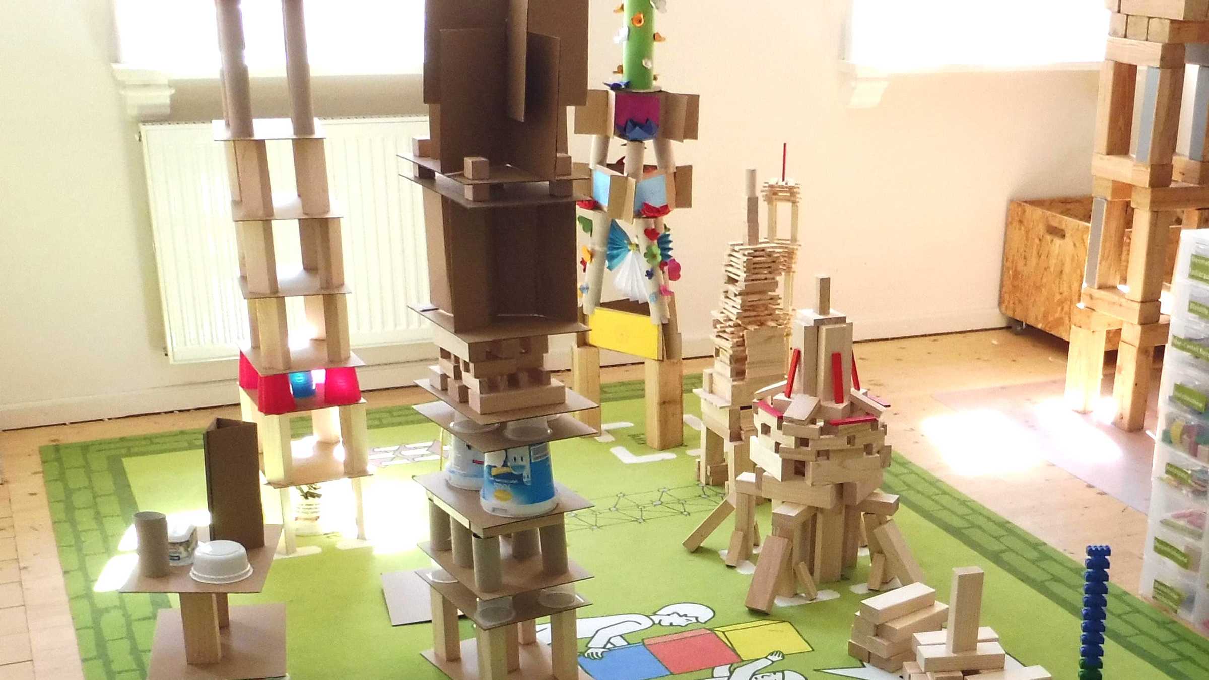 verschiedenen Türme aus Holzklötzen und Papprollen auf einem Spielteppich