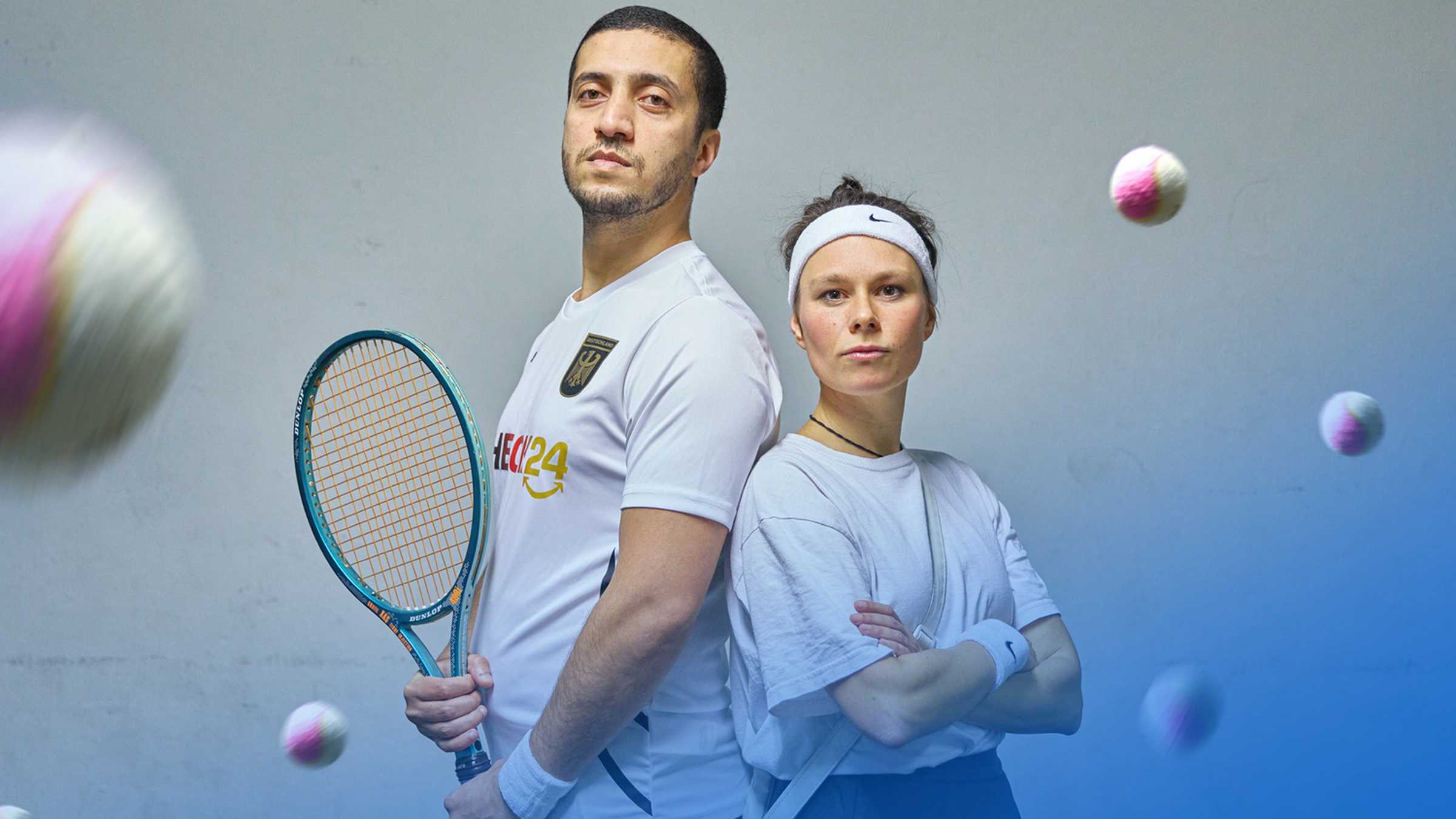 ein Mann und eine Frau in Tenniskleidung stehen Rücken an Rücken und schauen in die Kamera
