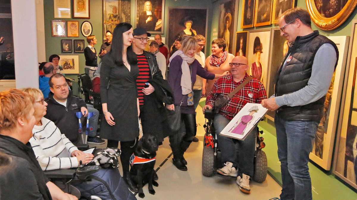 ein Ausstellungsraum mit vielen Menschen, die eine Führung verfolgen. Sie betrachten ein Bild, dass von der Führung gezeigt wird