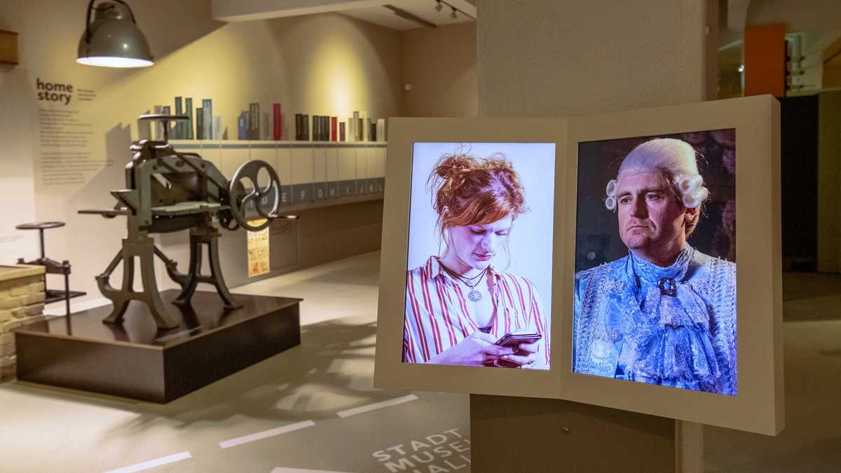 Ausstellungsraum mit Fotos von zwei Menschen. Im Hintergrund eine Druckmaschiene