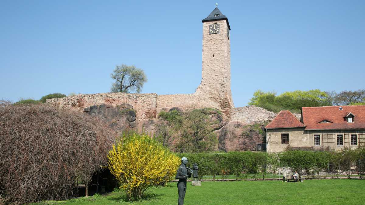 Die Oberburg Giebichenstein Etwas entfernt ist der Turm der Oberburg Giebichenstein zu sehen. Im Vordergrund steht auf einer grünen Wiese die Statue eines Mannes.