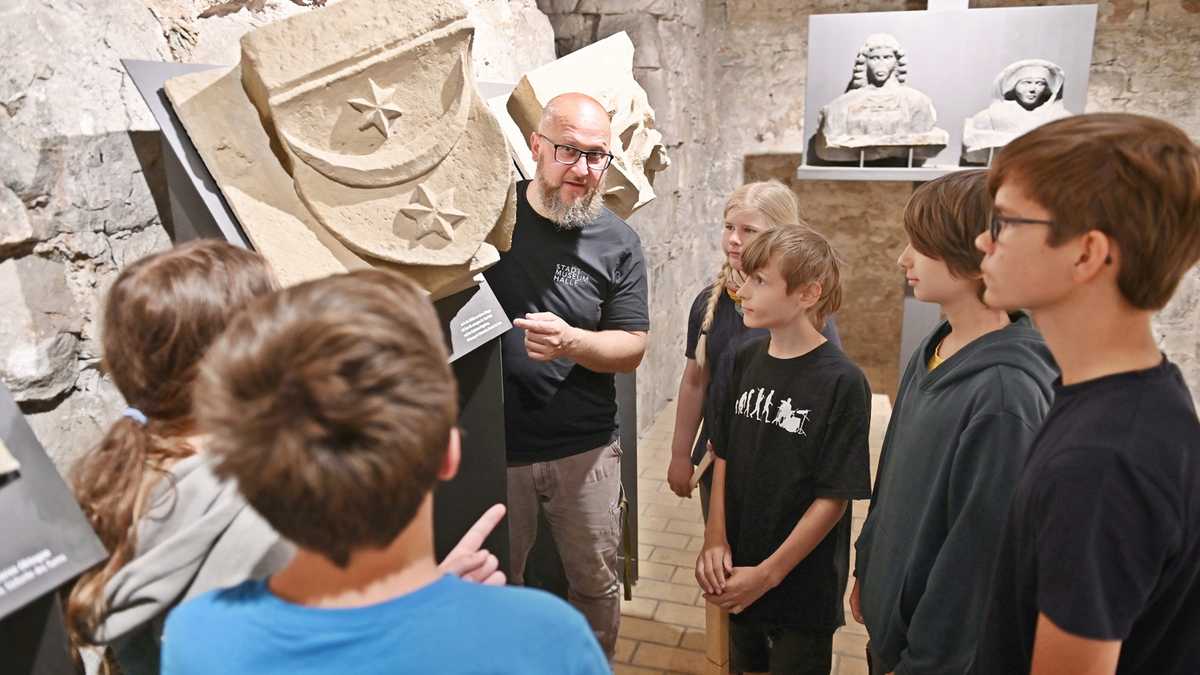 Mann präsentiert Jugendlichen ein steinernes Stadtwappen von Halle