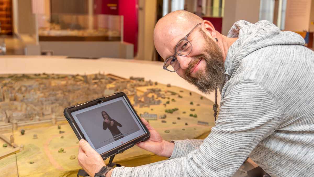 Henry Niekrawietz mit App Henry Niekrawietz mit einem Tablet, auf dem eine DGS-Führung gezeigt wird, im Stadtmuseum vor einem Stadtmodell