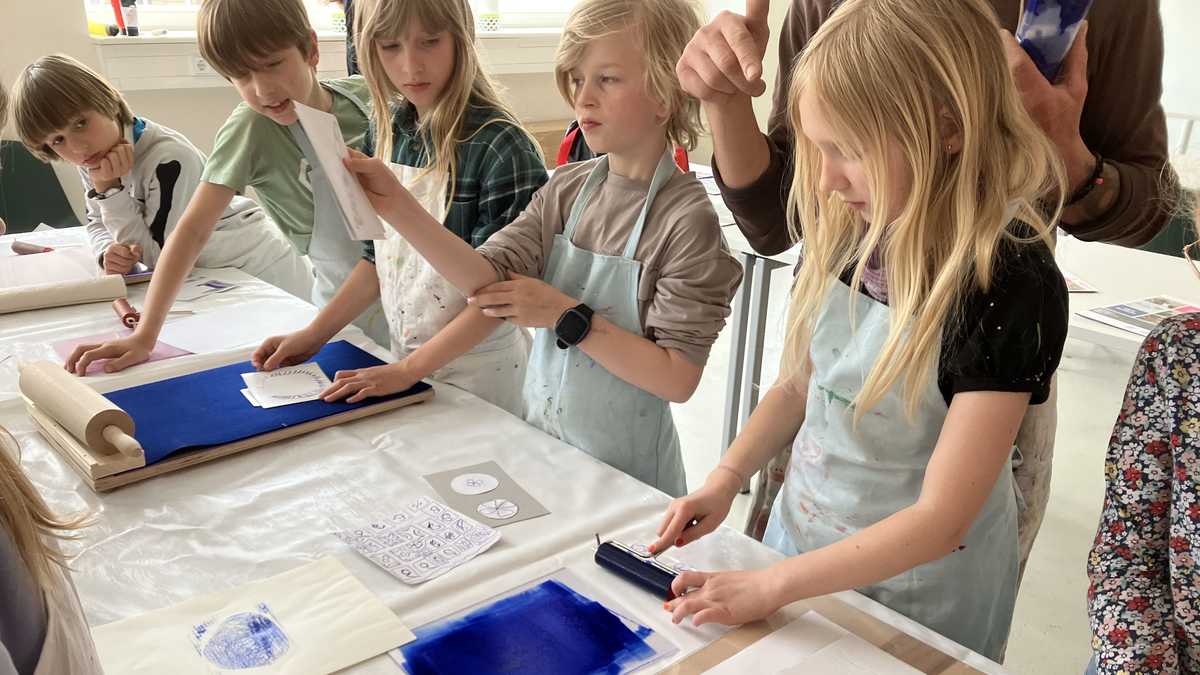 Druckworkshop eine Gruppe von Grundschulkindern steht am Tisch und probiert verschiedene Stufen des Druckvorgangs