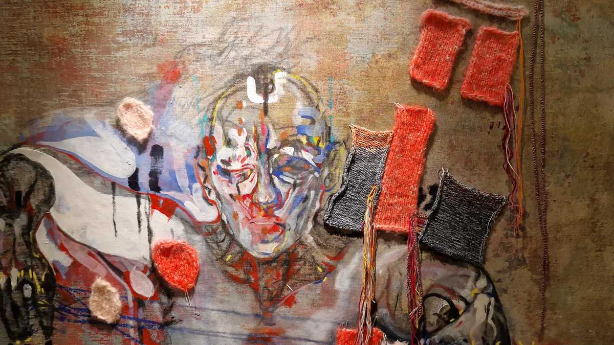 abstrakt gemalter Männerkopf, von gestrickten Applikationen rechts und links davon