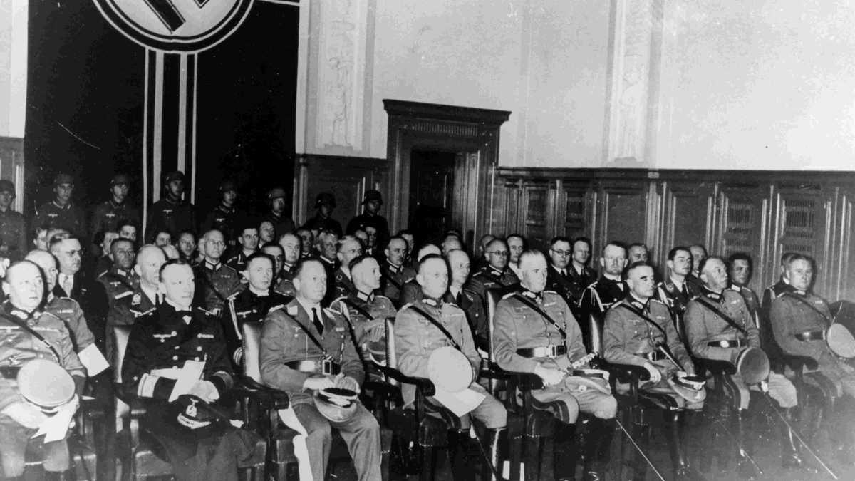 Gründungsveranstaltung Reichskriegsgericht Blick in einen Veranstaltungssaal mit Stuhlreihen, auf denen Männer in Nazi-Uniformen sitzen. Im Hintergrund eine Hakenkreuzfahne