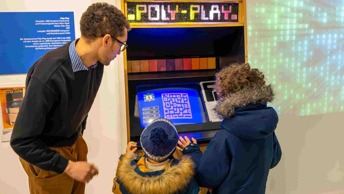 zwei Kinder und ein Mann am Spielautomat Poly-Play