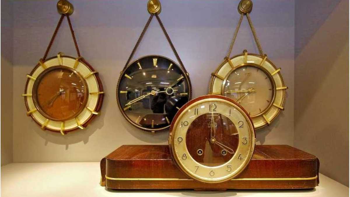 Drei Uhren im Hintergrund an der Wand aufgehängt davor eine Uhr stehend auf der Bdenplatte.