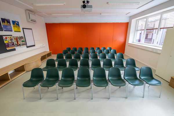Blick in einen Seminarraum mit vielen Stühlen. Ein oranger Schrank im Hintergrund