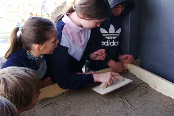 Drei Kinder streichen zusammen den Sand als Isolierung im Holzrahmen des zukünftigen Backofens glatt