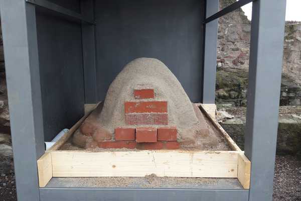 Die erste Kuppel des Lehmbackofens in seiner Überdachung ist zu sehen. Die Öffnung der späteren Backfläche ist voller Ziegelsteine zur Stabilisation der Lehmkuppel.
