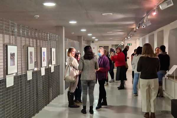 Viele Frauen stehen in der Fotoausstellung und sprechen miteinander. An einer offenen Gitterwand hängen gerahmte Fotos.