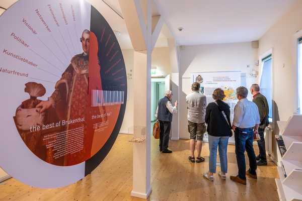 Fünf Personen stehen vor einem Roll-Up in der Brukenthal-Ausstellung. Links im Bild ist ein Ausstellungsobjekt, dass zur Interaktion einlädt.