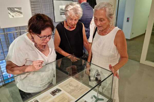 drei ältere Frauen beugen sich über eine Vitrine mit einem Fotoapparat und Dokumenten