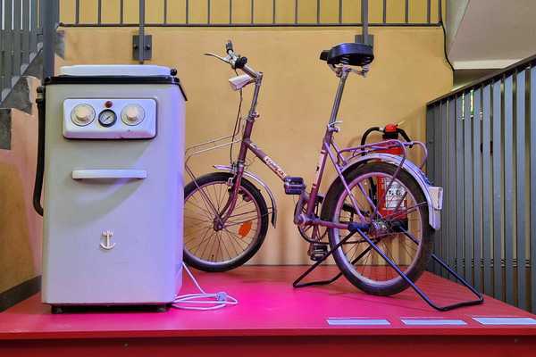 altmodische Waschmaschine und Klappfahrrad im Treppenhaus zum Ausstellungsraum