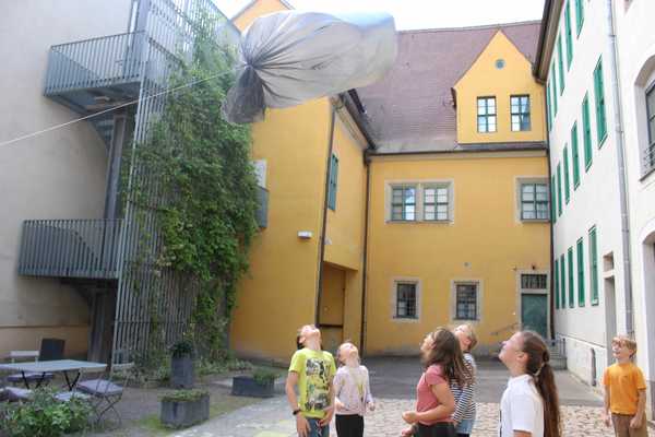 7 Kinder schauen auf dem Museumshof einem aufgestiegenen Plastiksack nach 