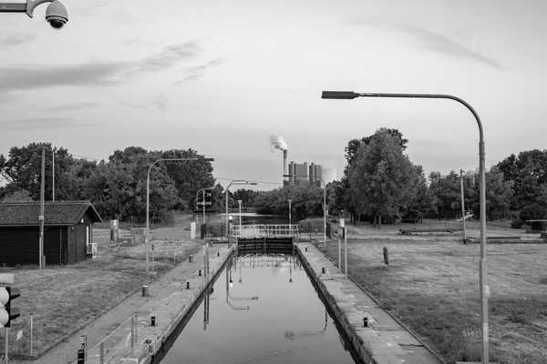 Blick vom Schleusentor auf das Schleusenbecken, im Hintergrund rauchende Schornsteine einer Industriealage