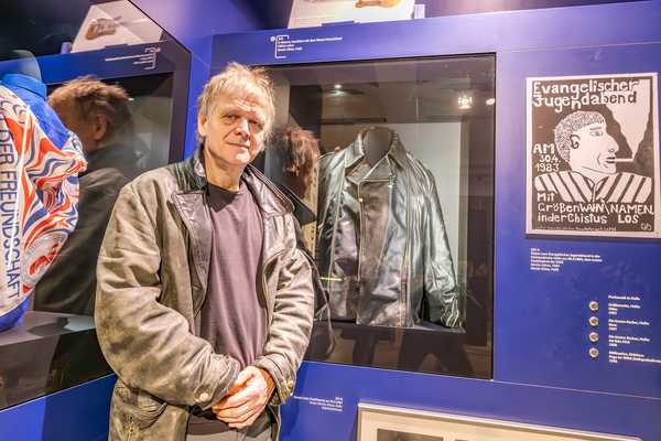 Moritz Götze vor steht vor seinen Objekten in der Dauerausstellung: einer schwarzen Lederjacke und einem Konzertplakat