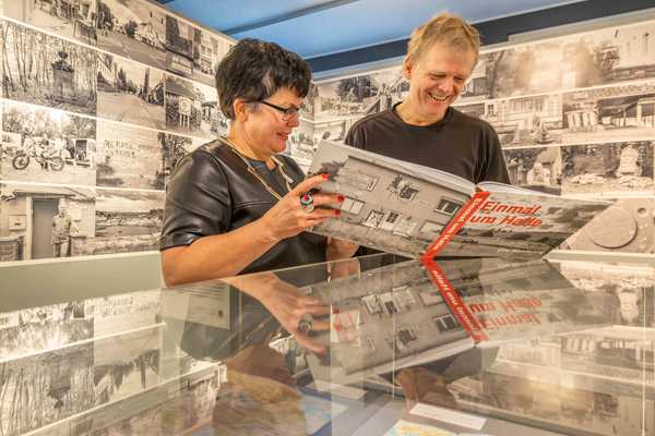 Jane Unger und Moritz Götze schauen sich lachend gemeinsam das Buch "Einmal um Halle" im Ausstellungsraum an