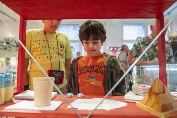Der Junge sieht sich eine Ausstellung "Spiel weiter!" an. Vor ihm stehen die Brettspiele.