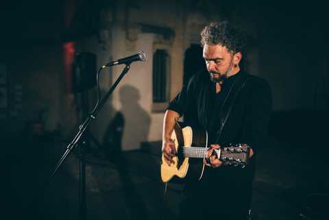 Bastian Bandt Bastian Bandt mit Gitarre und Mikrofon auf der Bühne. Das Licht wirft seinen Schatten auf die Wand