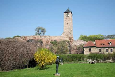 Die Oberburg Giebichenstein Etwas entfernt ist der Turm der Oberburg Giebichenstein zu sehen. Im Vordergrund steht auf einer grünen Wiese die Statue eines Mannes.