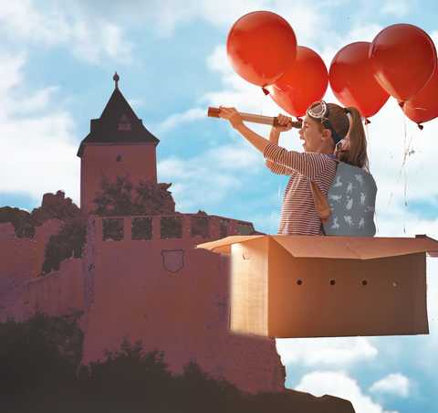 Burg Giebichenstein Grafik mit Burgsilhouette, im Vordergrund fliegt ein Mädchen in einem Ballon vorbei, der aus einem Pappkarton mit Luftballons besteht