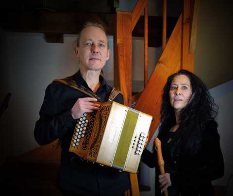 Sveriges Vänner Gudrun Selle mit Blockflöte und Johannes Uhlmann mit Akkordeon stehen vor einer Holztreppe.
