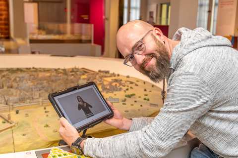 Henry Niekrawietz mit App Henry Niekrawietz mit einem Tablet, auf dem eine DGS-Führung gezeigt wird, im Stadtmuseum vor einem Stadtmodell