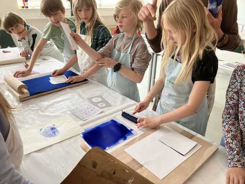 Druckworkshop eine Gruppe von Grundschulkindern steht am Tisch und probiert verschiedene Stufen des Druckvorgangs